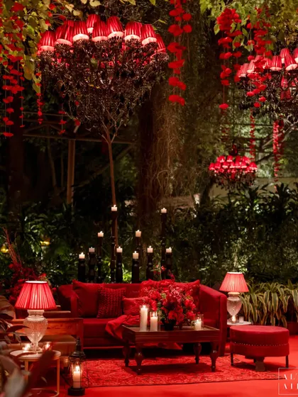 An intimate seating nook at the 'Laal Bagh' reception, bathed in red light from custom chandeliers and table lamps. The entire space was designed to feel like a luxurious, historical escape.