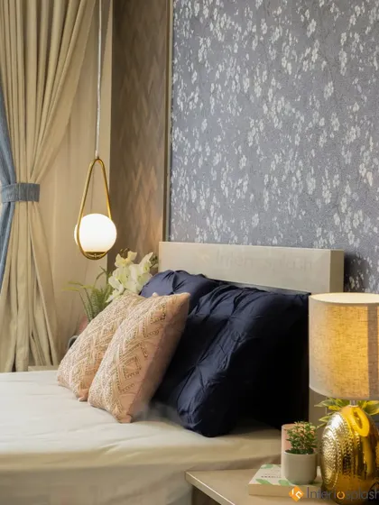 A close-up of the bedside, showing the mix of textures with the patterned pillows, the soft glow of the lamps, and the floral wallpaper.