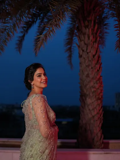 A profile shot against the evening sky, highlighting the delicate hairstyle and the sheer, embellished fabric of the saree.