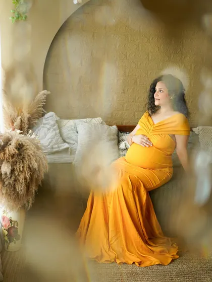 A dreamy solo portrait of the mother-to-be in a golden-yellow gown, seated in our boho-chic studio.