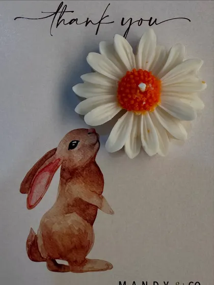 The orange and white daisy candle paired with our cute bunny-themed card. It smells like fresh roses and looks like a little piece of sunshine.