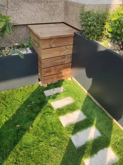 The finished wooden cover, neatly concealing a utility pipe on the terrace. It blends in with the artificial grass and stepping stone path, showing how practical problems can have beautiful solutions.