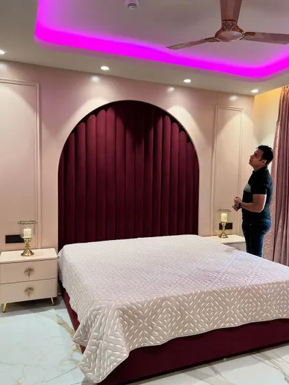 This bedroom features a stunning arched headboard in deep red velvet, set against a blush-pink paneled wall. The pink cove lighting adds a soft, glamorous glow to the room.