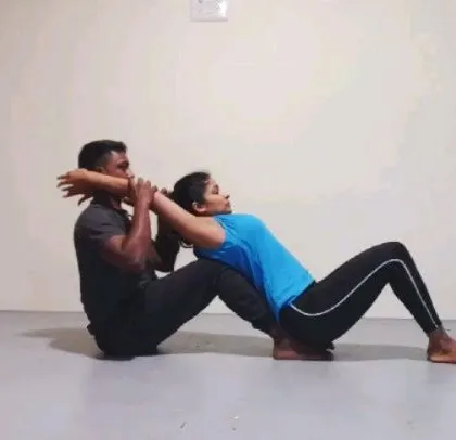 This is an assisted backbend, a preparation for Kapotasana (Pigeon Pose). I'm helping my student open her thoracic spine by providing stable support, allowing her to relax into the stretch.