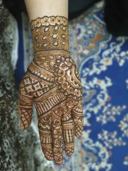 This intricate wrist and hand design features peacock-inspired motifs and delicate net patterns. It's a beautiful example of detailed henna artistry for a special event.