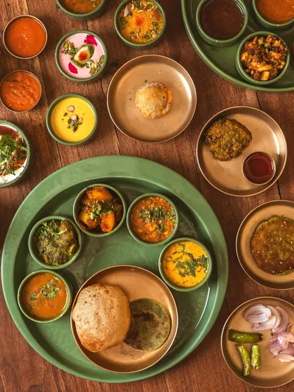 A beautifully styled traditional Indian thali. The overhead perspective and organized arrangement of various bowls, puris, and chutneys create a visually rich and appealing image for showcasing authentic cuisine.