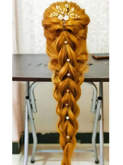 A long, flowing pull-through braid decorated with small floral pins, a popular style for modern brides.