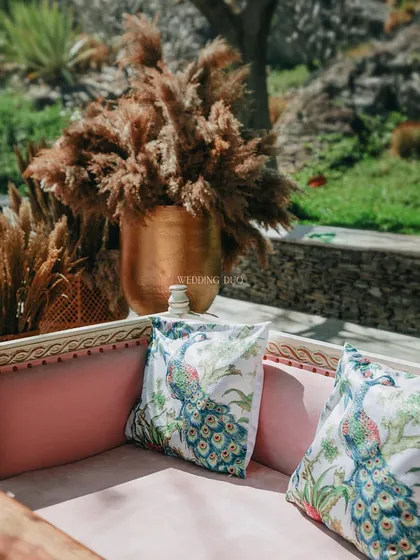 It's the little details that make a day unforgettable. For this event, we used custom-printed peacock cushions on a pink velvet sofa, set next to a large brass vase fatores pampas grass.