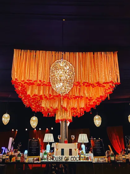 A dramatic and luxurious bar design featuring a massive orange and gold tassel chandelier. The lighting and decor elements are designed to create a high-end, celebratory mood.