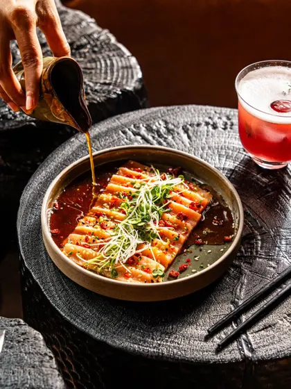 Salmon carpaccio with a sauce being poured. This dynamic shot captures the final touch being added to the dish, highlighting its freshness and elegant preparation.