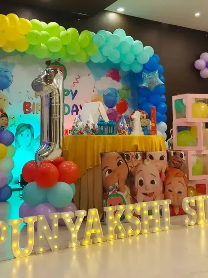 A full view of the Cocomelon first birthday setup for Punyakshi. The decor includes a rainbow balloon arch, character cutouts, and a light-up name, creating a vibrant and fun atmosphere.