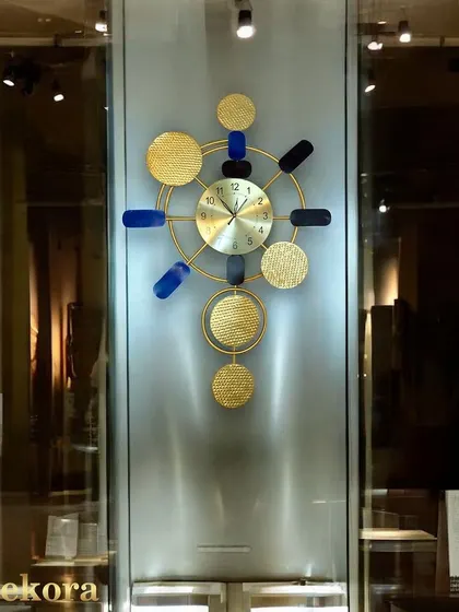 An elegant and modern wall clock featuring textured gold discs and bold blue accents, perfect for a sophisticated office or hotel lobby.