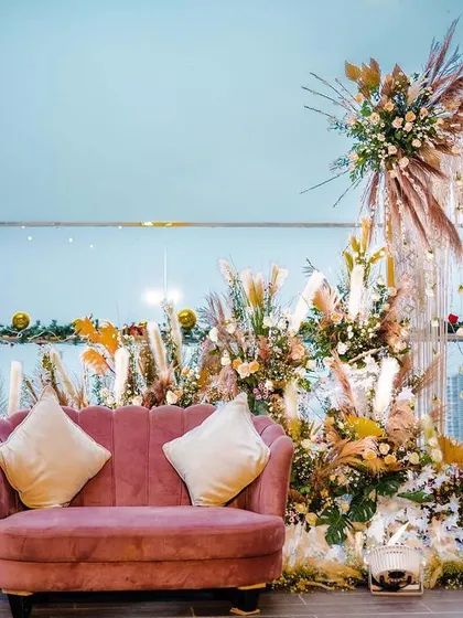 A bohemian-chic photo booth setup against a city skyline. The design uses a dusty rose sofa, pampas grass, and dried floral elements to create a stylish and relaxed atmosphere perfect for a modern brand activation.