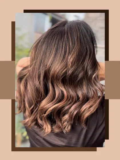 A beautiful shot of a balayage with warm brown and light caramel tones. The hair is styled in soft, beachy waves.