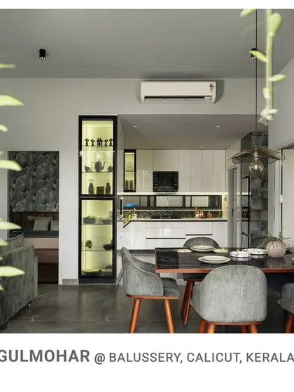The open-plan living and dining area at Gulmohar, seen through a frame of indoor plants, showcasing a modern, integrated space with views of the garden.
