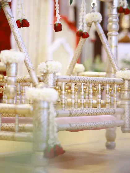 A detailed shot of the ornate silver-coated cradle, adorned with delicate white flowers and hanging red rose buds.