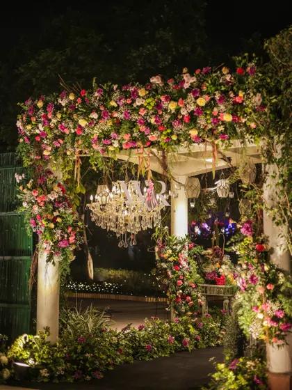 A beautiful floral archway with a chandelier hanging in the center. The mix of colorful flowers and lush greenery creates a romantic and picturesque frame.
