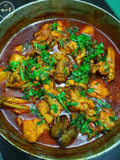 A large pot of chicken curry garnished generously with fresh coriander.