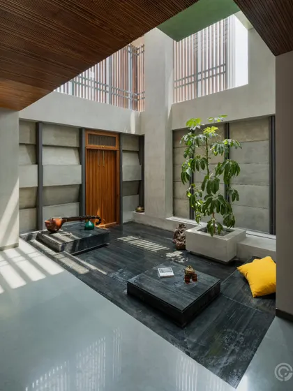 This internal courtyard features a floor of dark, locally sourced stone, which grounds the space. The surrounding walls are made of textured concrete blocks, creating a rich material palette that is animated by the play of natural light.