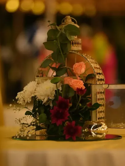 A close-up of a romantic table centerpiece featuring a vintage-style birdcage filled with fresh flowers, set on a mirrored base to reflect the soft, ambient light.