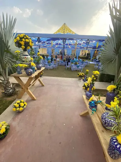 The entrance path to the "Jaipuri Blue Pottery" Mehendi, lined with wooden tables displaying an array of themed floral arrangements.