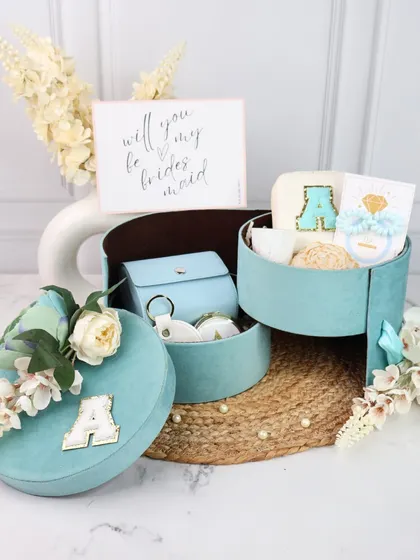This unique three-tiered bridesmaid proposal box in a stunning teal color is designed to wow your friends. It opens up to reveal different personalized items in each compartment, including a monogrammed jewelry case and other accessories.