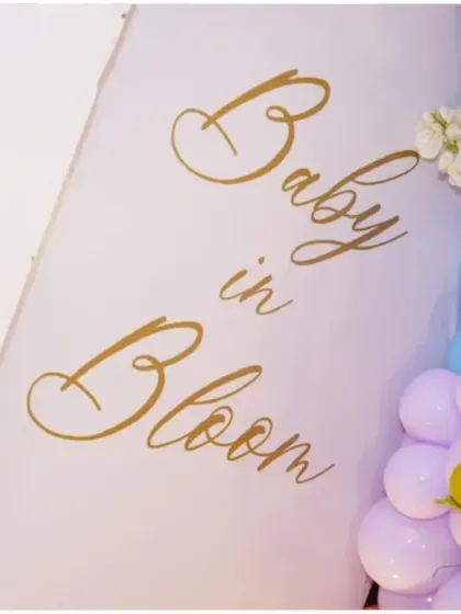 A close-up of the 'Baby in Bloom' sign from a butterfly-themed baby shower. The gold calligraphy adds an elegant touch.
