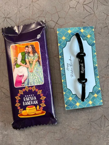 A simple yet personal Rakhi gift combo. It includes a chocolate bar with a custom photo wrapper and a bracelet-style rakhi with the brother's name.