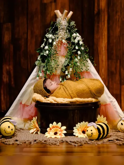 A newborn rests peacefully in a bucket, set against a beautifully decorated teepee, part of our charming "bumblebee" theme.