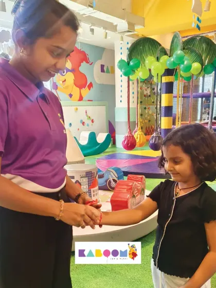 A staff member gently ties a friendship band onto a little girl's wrist, a sweet moment from our Friendship Day event filled with games and crafts.