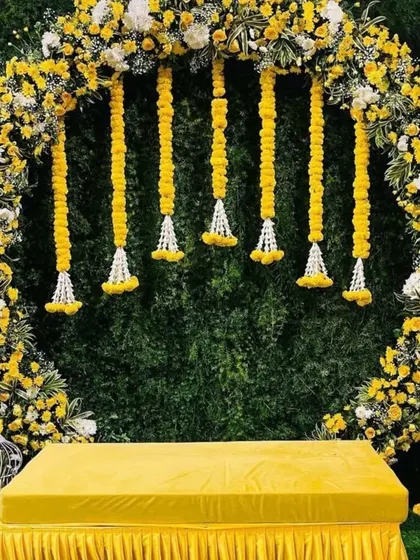 A modern take on Haldi decor is always so much fun. This setup features a full circular arch covered in yellow and white flowers against a lush green wall, creating a fresh and elegant backdrop for photos.