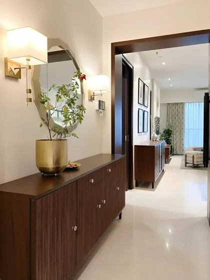 An elegant and classic hallway with a dark wood console table and a large octagonal mirror. The wall sconces provide warm, ambient lighting.