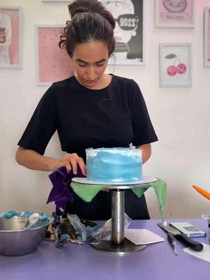 Another angle of me working on the watercolor cake. You can see my tools and colors on the table, ready for the next step.