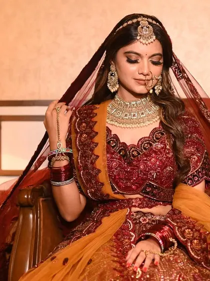 A full portrait of the bride seated, showcasing the flow and detail of her dupatta and lehenga.