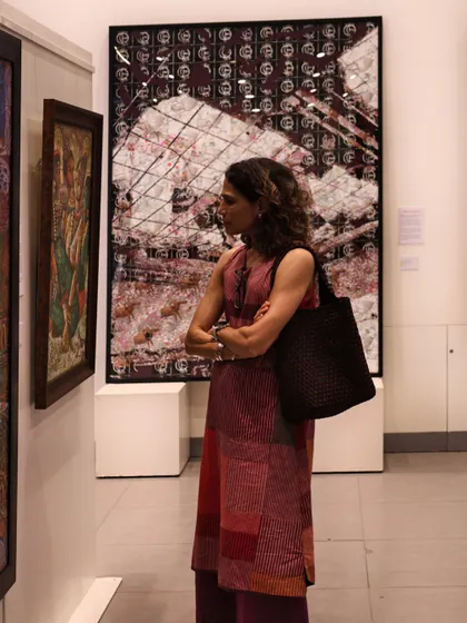 A visitor studies a painting, with Avinash Veeraraghavan's large-scale digital work 'Underworld Belly Button' visible in the background. The exhibition brings together a vibrant mix of artists and art lovers.