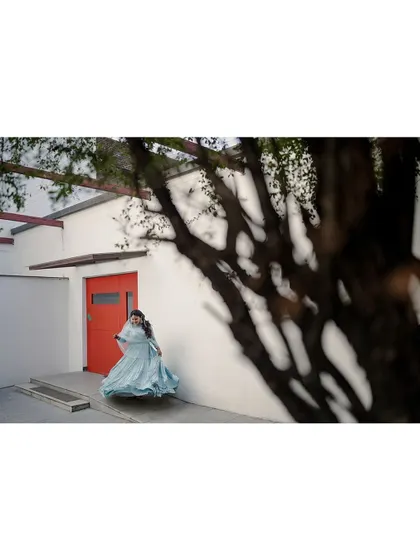 A wide shot showing the bride in her flowing gown against a minimalist background, with a tree's shadow creating an interesting visual frame.