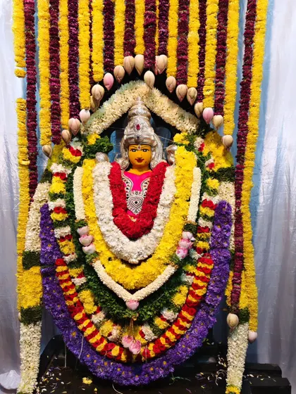 A deity at Vasavi Matha Temple adorned with elaborate, multi-layered garlands of fresh flowers and lotus buds.