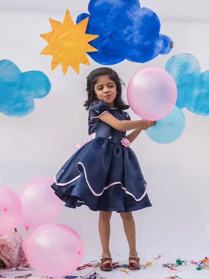 This navy blue party dress is all about movement and fun. The full skirt with pink trim is perfect for twirling, and the floral detail at the waist adds a sweet, feminine touch.