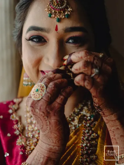 A close-up of the bride adjusting her nose ring, her smile hinting at her joyful anticipation. The shot highlights her beautiful henna and traditional ring.