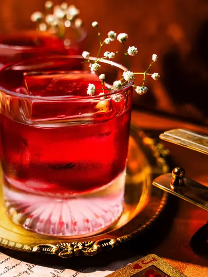 A close-up of a vibrant red cocktail at Baglami, garnished with baby's breath. The intense color and delicate flower create a beautiful contrast, shot with moody lighting to feel intimate and luxurious.