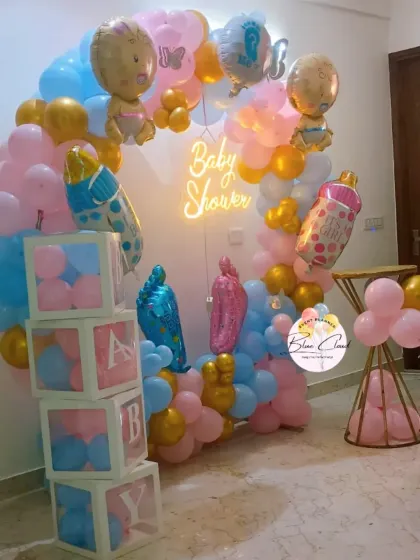 A vibrant gender reveal baby shower setup with a balloon ring, 'BABY' blocks, and a neon sign.