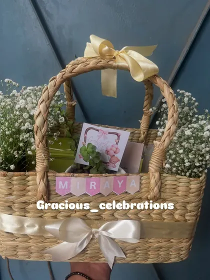 This beautiful cane basket was part of a 250-piece order for a first birthday. It's filled with a cake loaf, organic honey, cookies, a jade planter, and a scented candle, all decorated with fresh flowers.