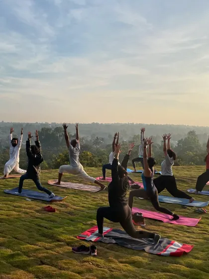 A group of participants in a deep lunge pose, stretching their hips and legs. The panoramic view of the misty morning landscape adds a layer of magic to the practice.