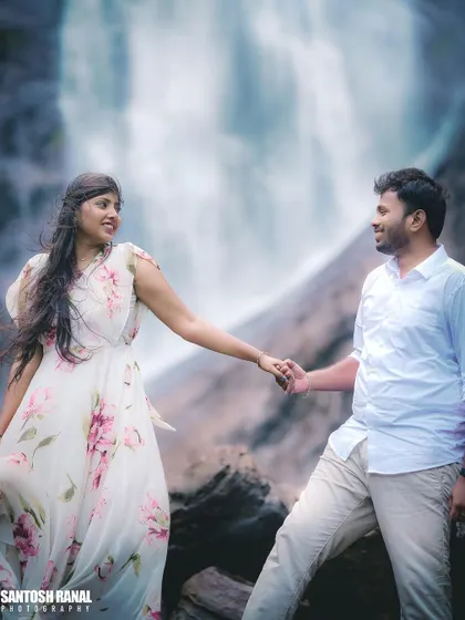 A tender moment of connection as the couple holds hands in front of a waterfall.