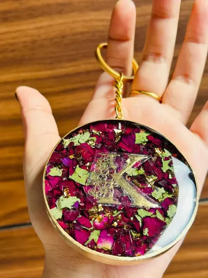 A personalized resin keychain with preserved rose petals and gold flakes, featuring a custom initial. This makes a beautiful and personal accessory.