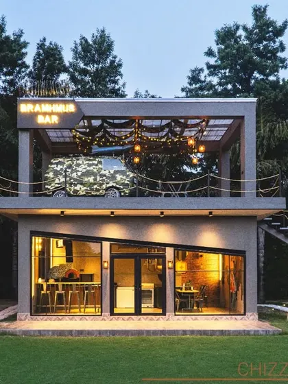 The Bramhmus Bar in Manesar is a unique indoor-outdoor concept I designed. The structure is a modern, two-story cube with large glass windows on the ground floor and an open-air terrace bar on top, complete with a decorative camouflage van.