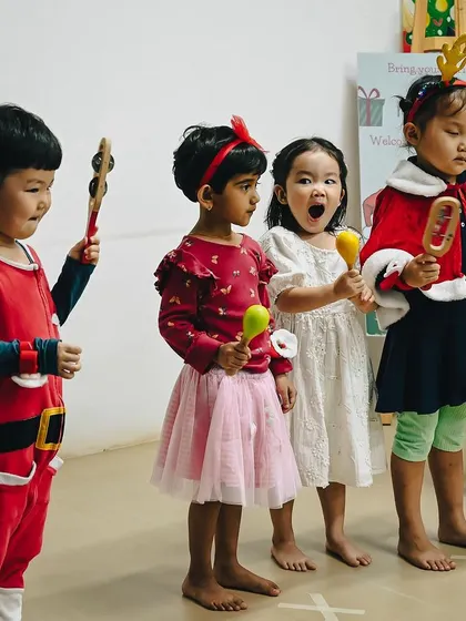 Children dressed in festive red outfits stand together, ready to perform at the Christmas party. They are holding musical instruments and singing with enthusiasm.