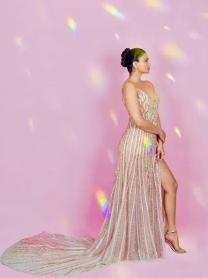 A profile view from the same series with Daisy Shah, emphasizing the flow of the gown's train and the elegant hair styling. The light flares add a touch of magic to the shot.