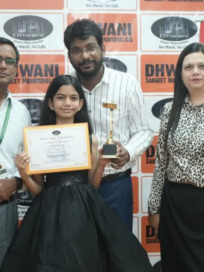 A young student receives her award from her teachers, with her mother looking on.