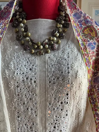 A close-up of the neckline, showcasing the dense Chikankari and mirrorwork embroidery, beautifully framed by the bold patterns of the Kashmiri Kalamkari dupatta.